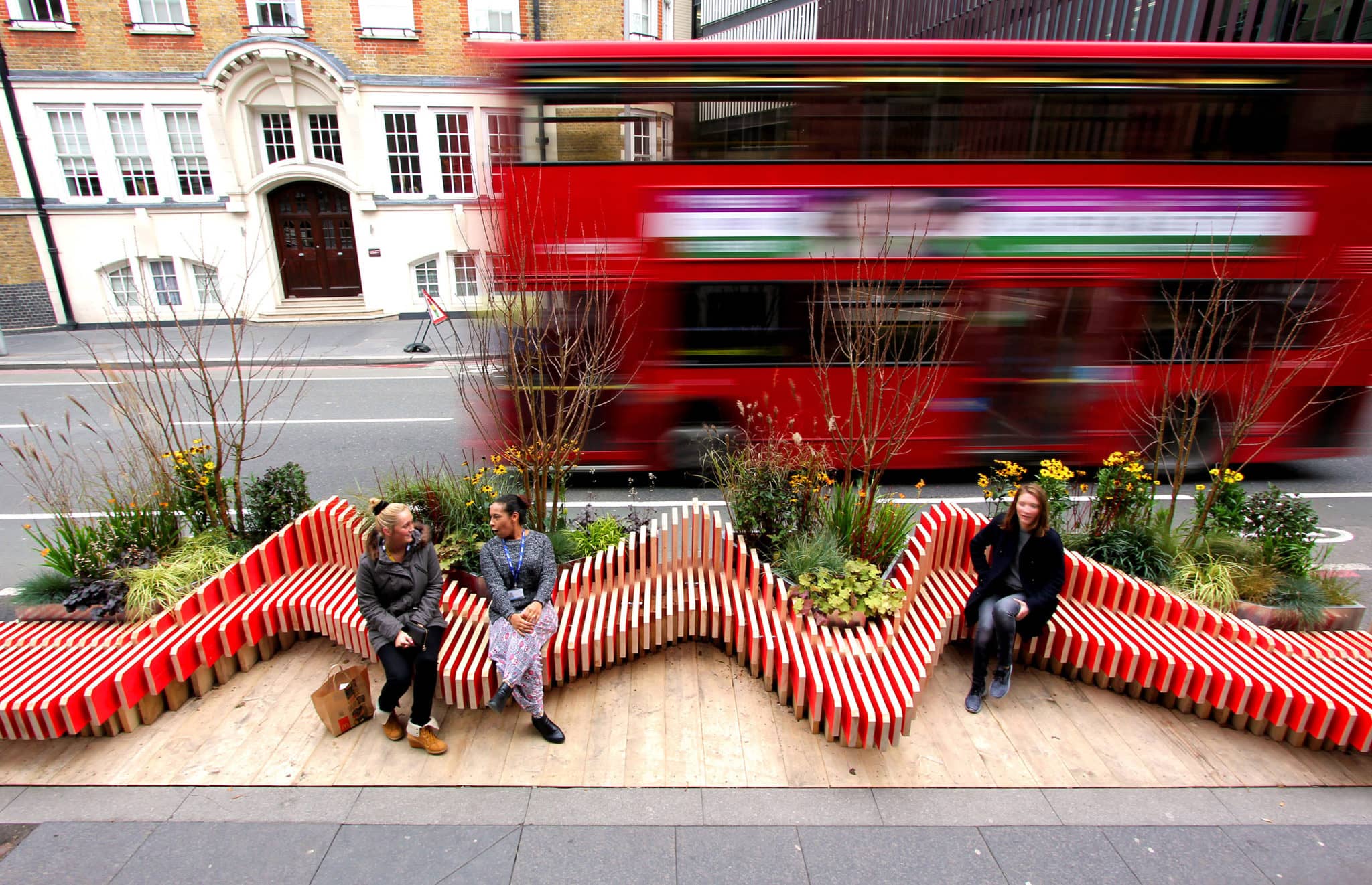 Exterior photography of a parametric zigzag continued public bench with people sitting on it; day mode bird-eye view.