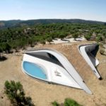 Exterior photography of a modern contemporary underground concrete house with a pool; day mode bird-eye view.