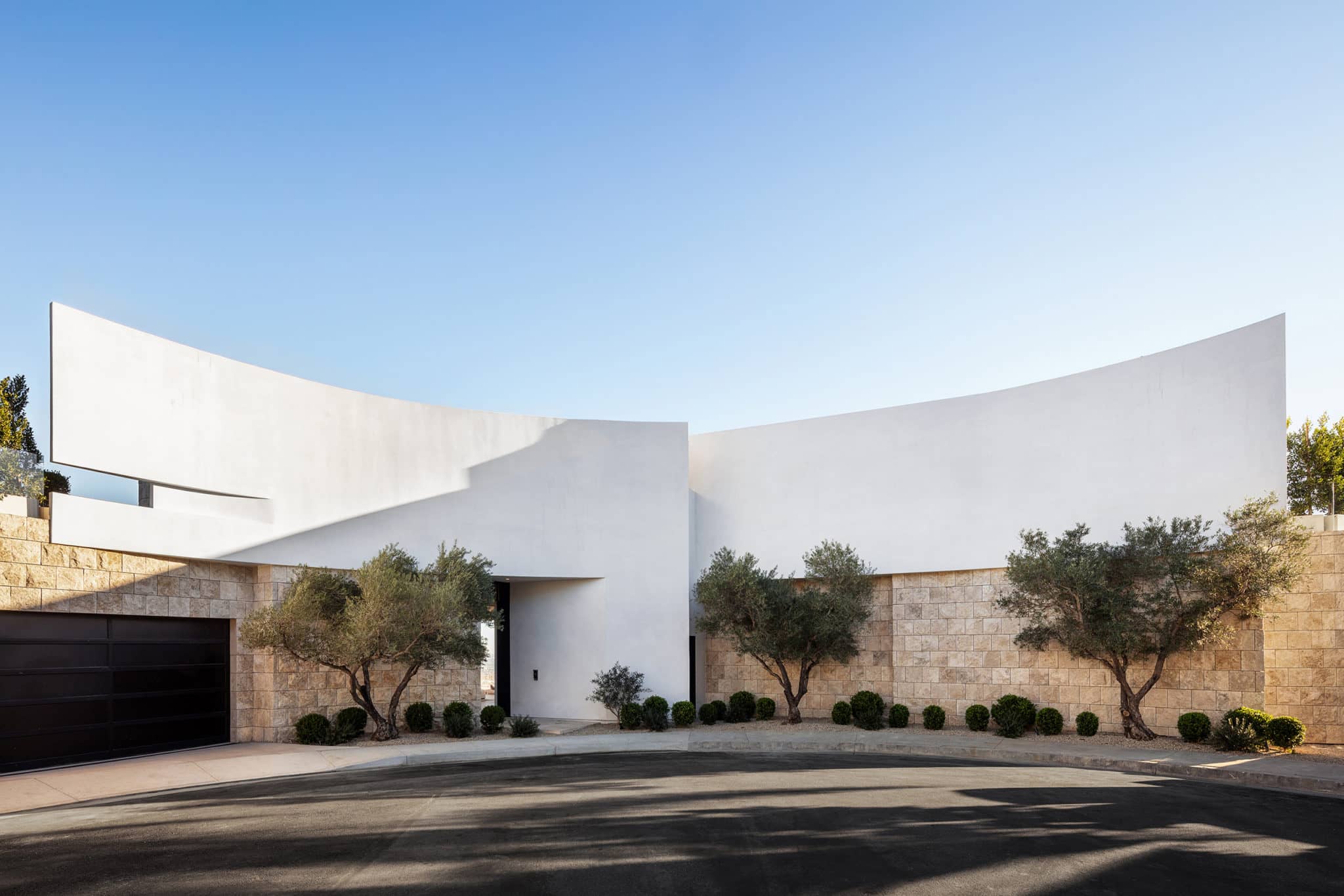 Exterior photography of entrance to a minimalist curved façade/house; day mode frontal street view.