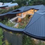 Exterior photography of a modern curved house roof and garden; day mode aerial view.