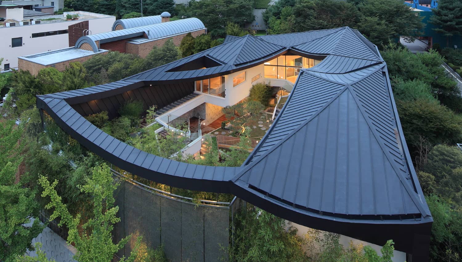 Exterior photography of a modern curved house roof and garden; day mode aerial view.