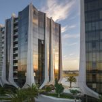 Exterior photography of residential glass façade towers with vertical elements; sunset view.