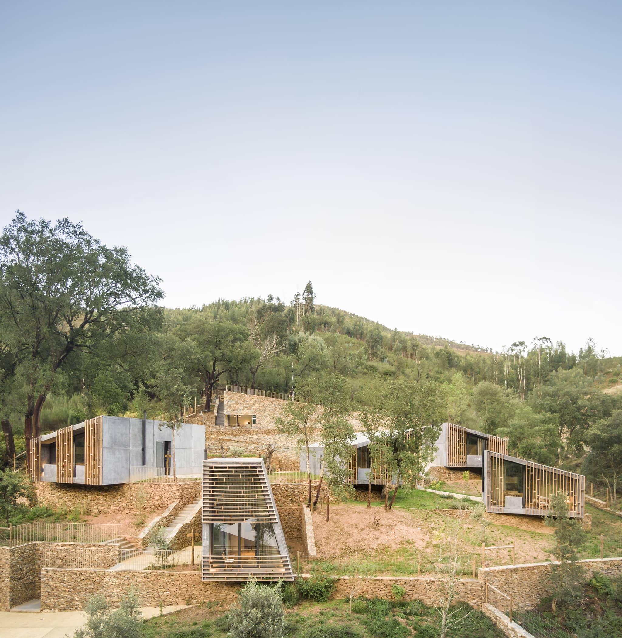 Exterior photography of minimalist concrete cabins; day mode frontal hillside view.