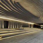 Interior photography of minimalist concrete mosque with stone walls, gradual scaled ceiling, and linear long steps with LED lights.