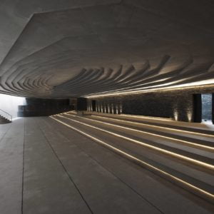 Interior photography of minimalist concrete mosque with gradual scaled ceiling with linear skylight, and linear long steps with LED lights.