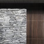 Exterior photography of a stone wall and wooden vertical blinds; day mode frontal view.